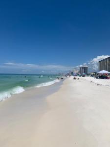 a white beach with people in the water and buildings at Tropical Haven in Panama City Beach