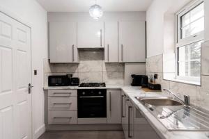 a white kitchen with a sink and a stove at Saxon House, sleeps 5, free parking in London