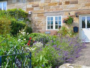 a garden in front of a stone house with flowers at Rowan Cottage in Aislaby