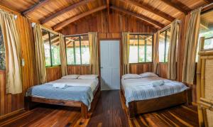 two beds in a room with wooden walls and windows at Kalea Yard Hotel in Puerto Jiménez