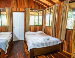 two beds in a room with wooden walls and windows at Kalea Yard Hotel in Puerto Jiménez
