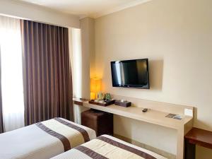 a hotel room with two beds and a desk with a tv at Bueno Colombo Hotel Yogyakarta in Kalasan