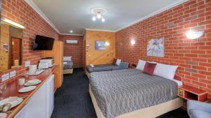 een kleine kamer met een bed en een bakstenen muur bij Elms Motor Inn in Tumut