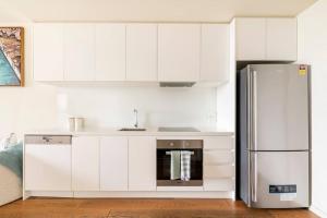 cocina con armarios blancos y nevera de acero inoxidable en Beachside flat with free parking en Melbourne