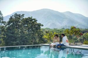 un uomo e una donna seduti sul bordo di una piscina di The Riverside Estate - 2Bedroom Private Pool Villa in Udaipur a Udaipur