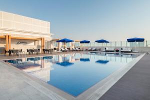 a swimming pool with chairs and umbrellas on a building at Riviera Rayhaan by Rotana Doha in Doha