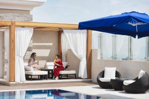 two women sitting on a patio next to a pool at Riviera Rayhaan by Rotana Doha in Doha