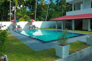 a pool with two chairs and umbrellas next to a house at Sayu Garden Hotel in Habaraduwa Central