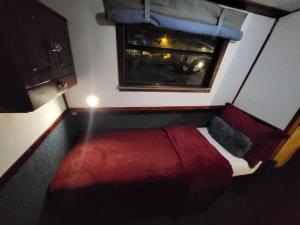 Cette petite chambre comprend un lit rouge et une fenêtre. dans l'établissement Comfy Canal Boat in London Centre Family & Friends, à Londres
