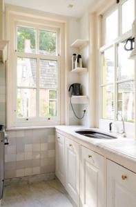 eine weiße Küche mit einem Waschbecken und 2 Fenstern in der Unterkunft Historical house on river Vecht in Maarssen
