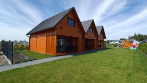 a wooden house with a yard with a playground at Słoneczne Chatki in Dziwnówek