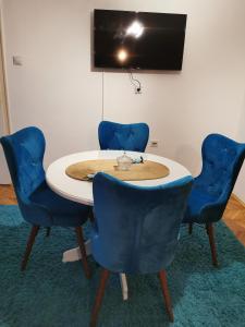 a table with four blue chairs and a tv on a wall at City Center Apartment JOTIC in Pirot