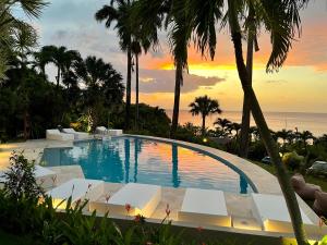 a swimming pool with palm trees and a sunset at Residence AU 'TI SUCRIER in Deshaies