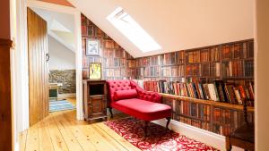 a red chair in front of a library with books at Mwsogl - Luxurious Family Fishing Lodge Near Aberaeron With Private Fishing in Cross Inn