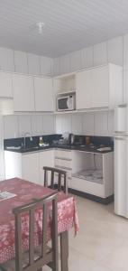 una cucina con mobili bianchi, un tavolo e un microonde di Casa na praia a Balneário Barra do Sul