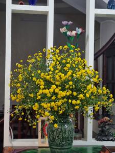 a green vase filled with yellow flowers on a table at May's Cottage in Hanoi