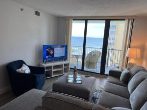 a living room with a couch and a tv and a balcony at Coastal Condo on the beach at Ocean Trillium #501 in New Smyrna Beach