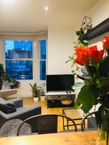 a living room with a television and a table with flowers at 20 min to central London- 2 bedrooms apartment in London