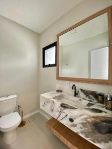 een badkamer met een wastafel, een toilet en een spiegel bij Bellacasa Rua Leão in Bombinhas