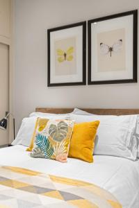 een slaapkamer met een bed met gele kussens en ingelijste foto's bij Notting Hill: Stylish 1BR with Terrace - Suite Inn in Londen