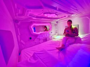 a woman sitting on a bed in a purple room at CAPSULE INN VALENCIA Hostel in Valencia