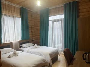 two beds in a room with green curtains and windows at Hotel ANNA PALACE in Khulo