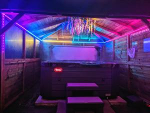 FINN VILLAGE "Raspberry Cottage" Private Garden, 6-seater Hot Tub, Firepit & Pizza Stove في غلاسكو: غرفة بها سرير مع أضواء أرجوانية وأزرق