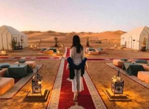 Merzouga Top Luxury Camp في مرزوقة: امرأة تقف في وسط الصحراء