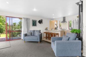 a living room with two chairs and a kitchen at Summer Haze - Omaha Holiday Home in Matakana