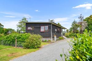 a black house with a gravel driveway at Summer Haze - Omaha Holiday Home in Matakana