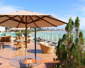 a patio with an umbrella and chairs and the ocean at AX Blue Suítes in João Pessoa