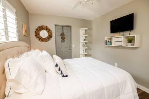 um quarto com uma cama branca e uma televisão de ecrã plano em Happy Camper Cottage - Cozy Oasis with Hot Tub em Palm Harbor