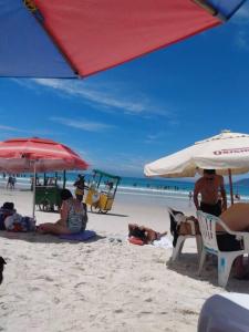 un grupo de personas sentadas en la playa bajo sombrillas en Ampla casa de praia em cabo frio, en Cabo Frío