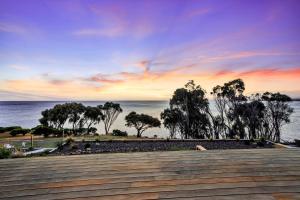 um pôr do sol sobre a água com árvores e um calçadão em Freycinet Coastal Retreat em Coles Bay