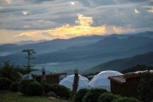 a group of four white tents with mountains in the background at เขาเเสงจันทร์ ม่อนเเจ่ม 4 in Mon Jam