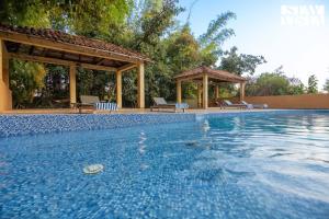 a swimming pool with chairs and a gazebo at StayVista's Rustic Respite - Hillside Retreat near Tala Gate with Swimming Pool, Lawn & Indoor-Outdoor Games in Tāla