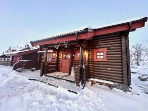 una cabaña de madera en la nieve con una puerta roja en Villa Tsahkal Kilpisjärvi en Kilpisjärvi