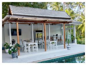 um pavilhão com mesas e cadeiras brancas e uma piscina em Ampha Place Hotel em Mae Nam