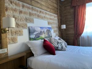 a bedroom with a white bed with a brick wall at Hotel Rododendro Val di Fassa in Campitello di Fassa