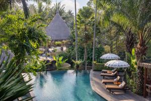 a pool at a resort with chairs and umbrellas at The Sankara Resort by Pramana in Ubud