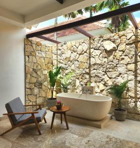 a bathroom with a bath tub and a stone wall at Motama Villa in Ubud