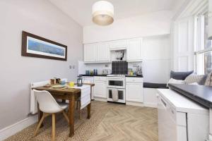 a kitchen with white cabinets and a wooden table with chairs at The Howard Apartment nr The Old Course in St. Andrews