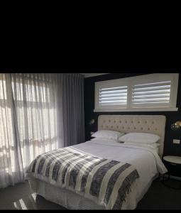 um quarto com uma cama grande com lençóis brancos e janelas em Inspire Boutique Apartments em Devonport