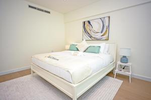 1BR Loft Soul Beach Escape - Mamsha Al Saadiyat في أبوظبي: غرفة نوم بيضاء مع سرير أبيض مع لوحة على الحائط