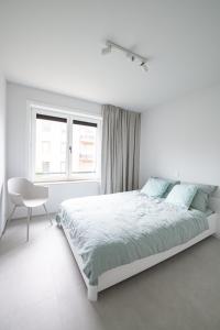 a white bedroom with a bed and a chair at Genieten in Groenendijk Oostduinkerke Koksijde - Vitamine Zee in Koksijde