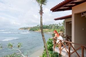 Una mujer parada en un balcón con vistas al océano en New Bay View Villa, en Weligama