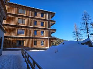 um edifício de madeira com neve em frente em Almappartement Nassfeld- Sonnenalpe em Sonnenalpe Nassfeld