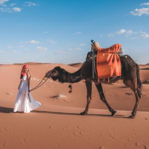 Uma mulher a passear um camelo no deserto em Merzouga Luxury Tent em Merzouga