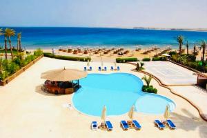 a swimming pool with chairs and umbrellas and the ocean at Apartment Sahl Hasheesh 1+1 in Hurghada