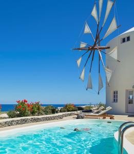 une piscine avec un parasol et l'océan en arrière-plan dans l'établissement Windmill Villas, à Imerovigli